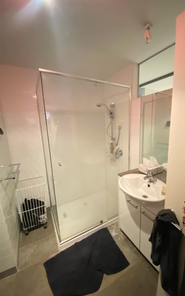 Photo of outdated bathroom with glass shower door, white bathroom sink and old cupboard before a bathroom renovation