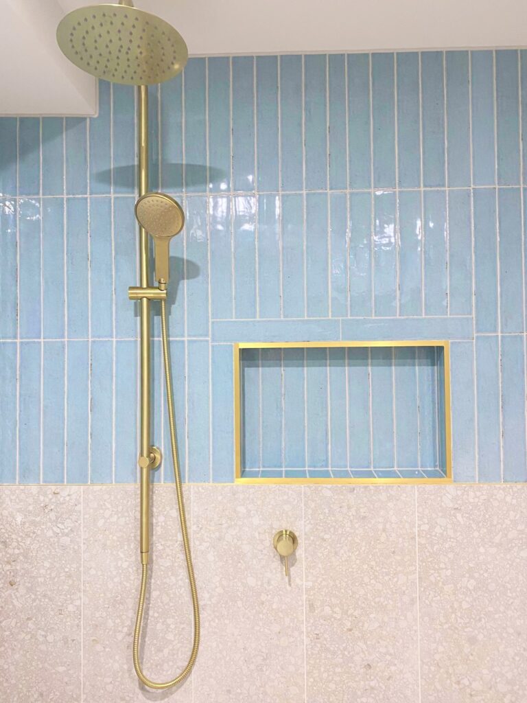 Bathroom renovation shower with brushed gold fixtures, blue subway style tiles and large beige tiling