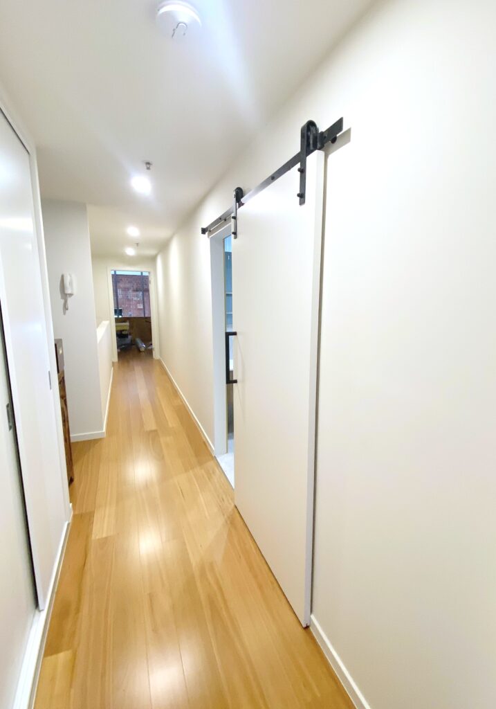 Fitzroy renovation project, long hallway with timber floorboards and sliding barn door to bathroom