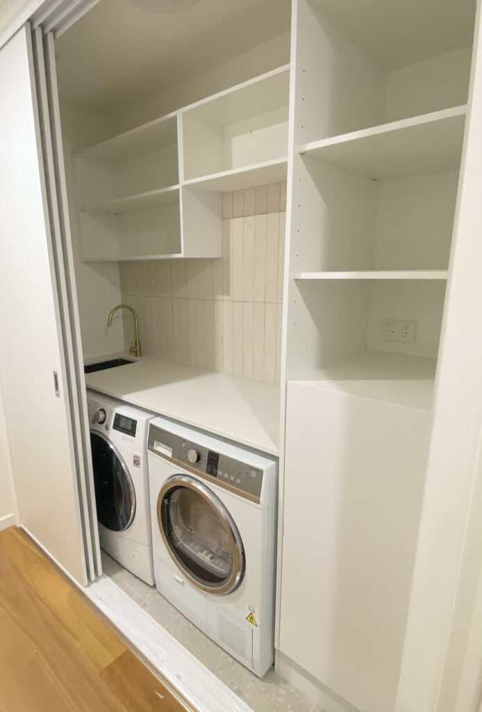 Compact European style laundry renovation containing sink, shelves and appliances behind sliding doors