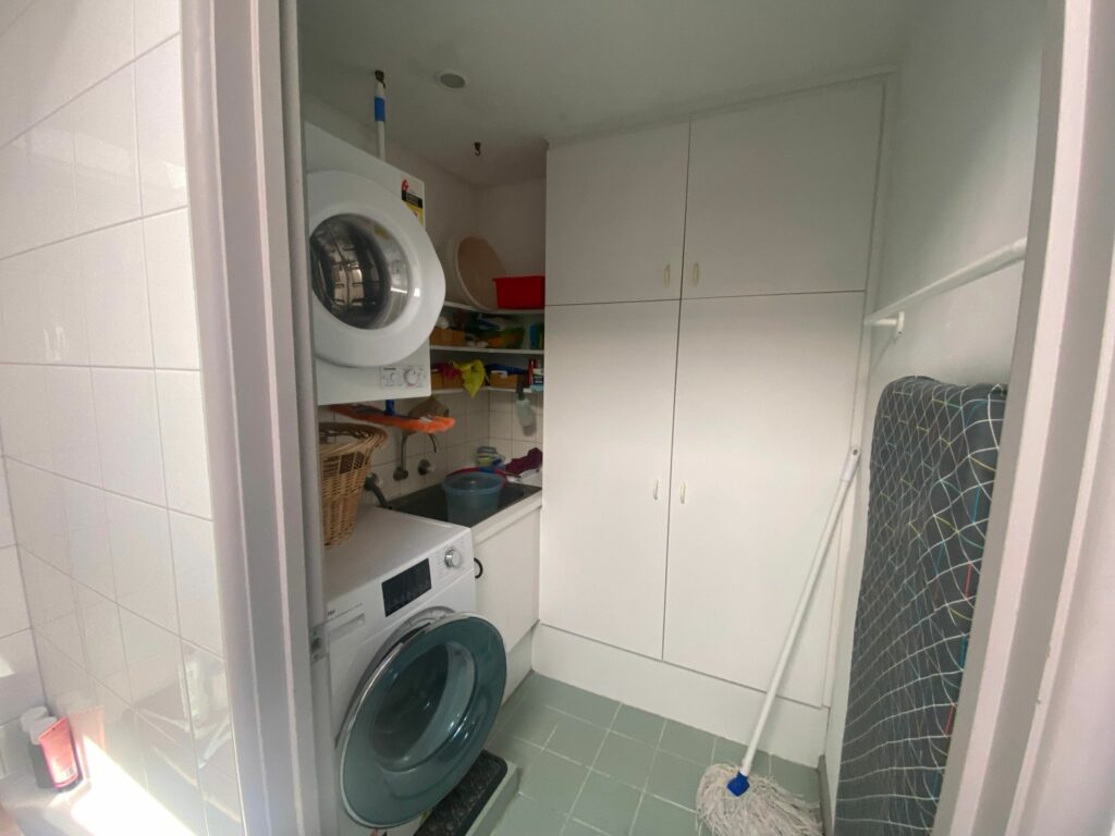 cluttered laundry room with washer and dryer and large white cupboard before laundry renovation in Carlton Victoria