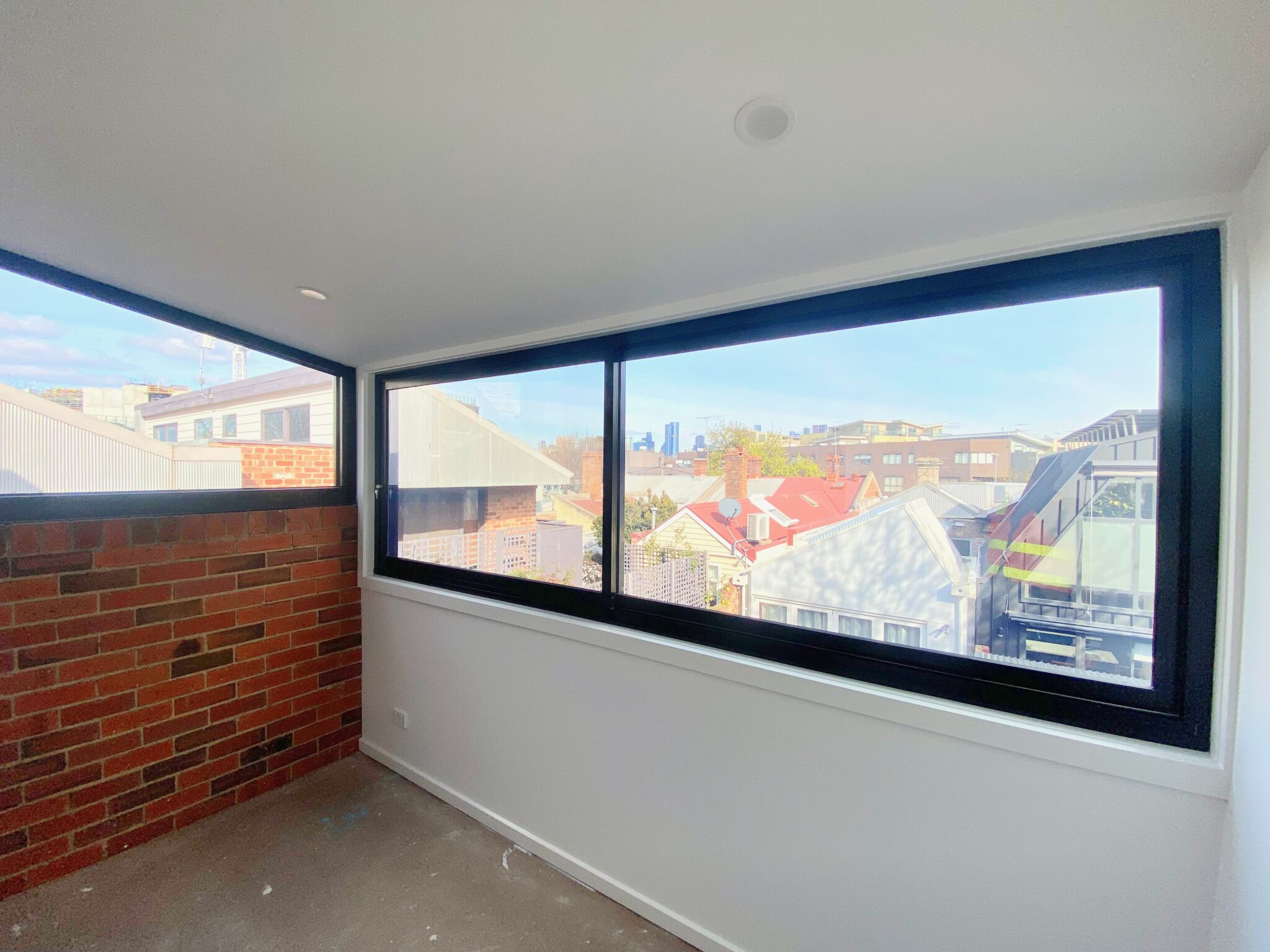 newly renovated room with red brick wall, large window showing view of Melbourne cityscape