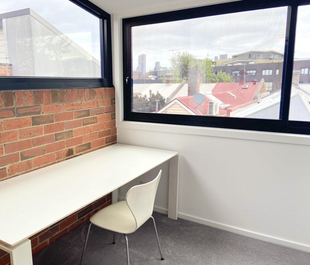 newly renovated room with red brick wall, large window showing view of Melbourne cityscape