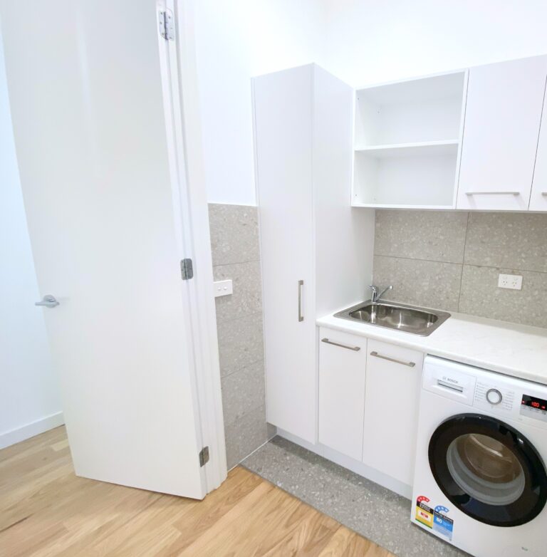 European style laundry renovation, with white cupboards, grey tiling and a washing machine