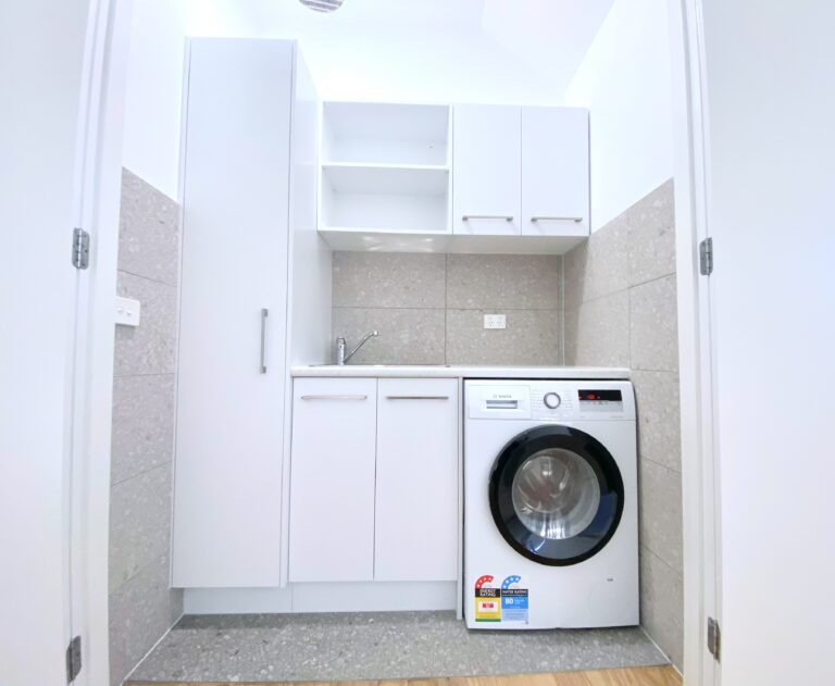 European style laundry renovation, with white cupboards, grey tiling and a washing machine